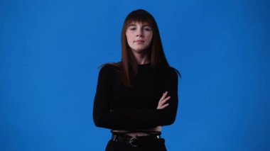 Kollarını kavuşturup mavi arka planda bir şeye negatif tepki veren bir kızın 4K videosu. Duyguların kavramı.