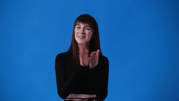 4K的慢镜头 一个女孩拍拍他的手 在蓝色的背景上微笑 情绪的概念 — 图库视频影像