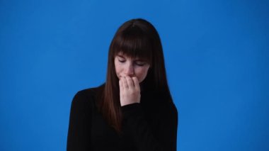 Mavi arka planda şüpheleri olan bir kızın 4K videosu. Duyguların kavramı.