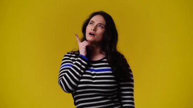 Bir kadının bir şey planladığını gösteren 4k 'lık video ve yukarı doğru sarı arka plana işaret ediyor. Duyguların kavramı.