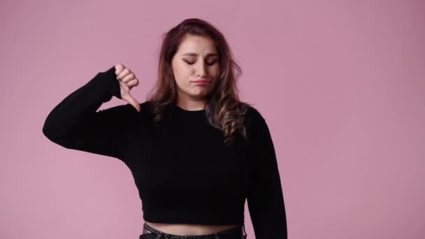 ピンクの背景に親指を下に示す否定的な顔の表情を持つ1人の女性の4Kビデオ 表現の概念 — ストック動画