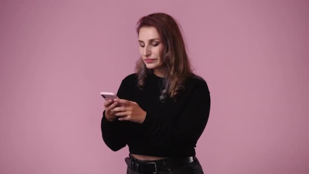 1人の女性がテキストを入力し ピンクの背景に笑みを浮かべての4Kビデオ 感情の概念 — ストック動画
