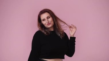 Gülümseyen ve saçlarını pembe arka planda düzelten bir kadının 4K videosu. Duyguların kavramı.