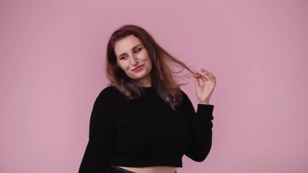 ピンクを背景に笑顔で髪を固定する1人の女性の4Kビデオ 感情の概念 — ストック動画