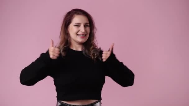 ピンク色の背景に親指を立てて微笑む1人の女の4Kスローモーションビデオ 感情の概念 — ストック動画