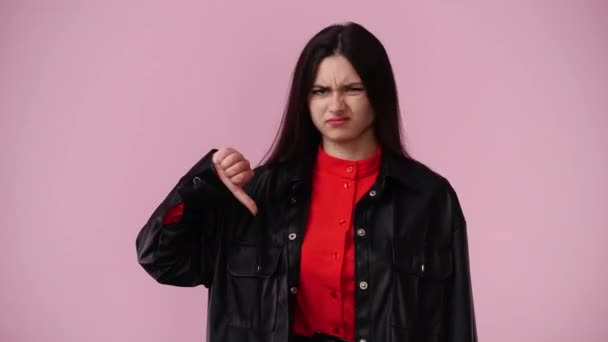 一个面部表情消极的女孩的4K视频 在粉色背景下显示大拇指朝下 情绪的概念 — 图库视频影像