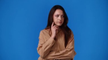 Bir kızın mavi arka planda elini çenesine dayayarak bir şeyler planladığını gösteren 4K video. Duyguların kavramı.