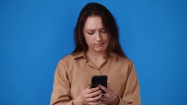 Sarı arka planda negatif yüz ifadesi olan bir kızın telefonda yazı yazarken 4K videosu. Duyguların kavramı.