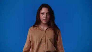 Mavi arkaplanı işaret eden bir kızın 4K videosu. Duyguların kavramı.