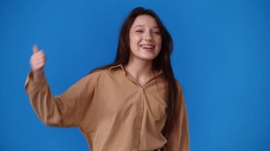 Mavi arka planda baş parmak gösteren ve gülümseyen bir kızın 4K yavaş çekim videosu. Duyguların kavramı.