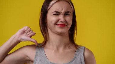 4k video of one girl with negative facial expression showing thumb down over yellow background. Concept of emotions.