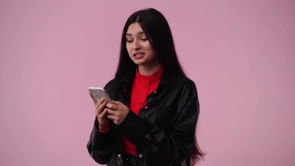 1人の女の子がテキストを入力し ピンクの背景で笑顔の4Kビデオ 感情の概念 — ストック動画