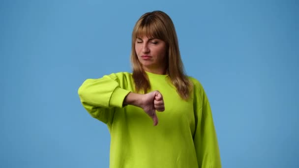 青い背景の上に親指を下に示す否定的な顔の表情を持つ1人の女の子の4Kスローモーションビデオ 感情の概念 — ストック動画