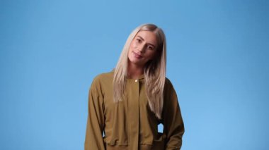 Mavi arka planda poz veren ve gülümseyen bir kadının 4K videosu. Duyguların kavramı.