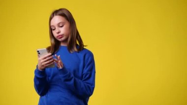 Bir kızın 4k yavaş çekim videosu sağı gösteriyor ve telefonu sarı arkaplanda elinde tutuyor. Duyguların kavramı.