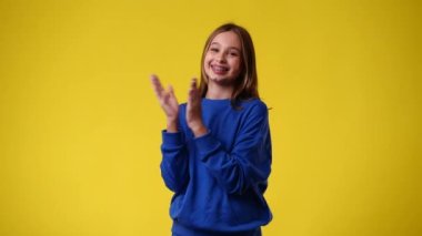 4k slow motion video of one girl claps his hands and smiling over yellow background. Concept of emotions.