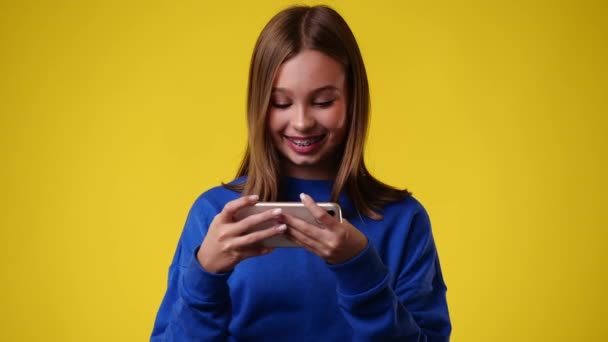 Video Van Een Meisje Speelt Aan Telefoon Glimlacht Gele Achtergrond — Stockvideo