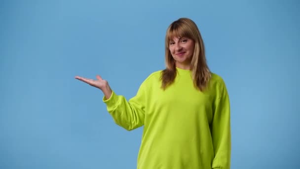 一个女人把手指指向左边 在蓝色背景下微笑的4K视频 情绪的概念 — 图库视频影像