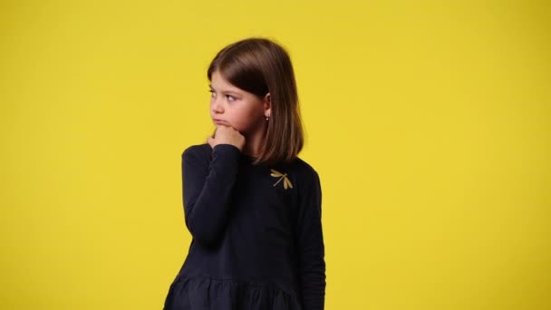 黄色い背景の上に手を顎に置くことで何かを計画している1人の子供の4Kビデオ 感情の概念 — ストック動画