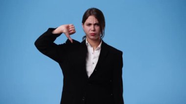 Negatif yüz ifadesi olan bir kızın mavi arka planda baş parmağını aşağı gösteren 4K videosu. Duyguların kavramı.