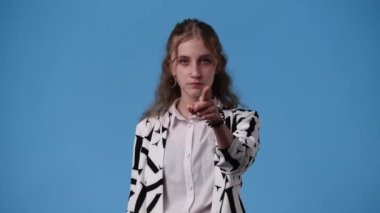 Mavi arka planda sessizlik işareti gösteren bir kızın 4K videosu. Duyguların kavramı.