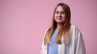 Pembe arka planda kurnaz yüz ifadesi olan bir kızın 4K videosu. Fikirleri olan kız kavramı.
