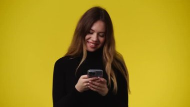 Sarı arka planda telefonunu kullanan bir kızın 4K videosu. Duyguların kavramı.