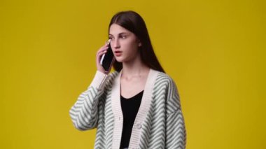 Sarı arka planda telefonla konuşan bir kızın 4K videosu. Duyguların kavramı.