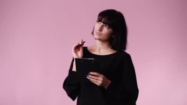 Pembe arka planda bir kalemle not alan bir kadının 4K videosu. Duyguların kavramı.