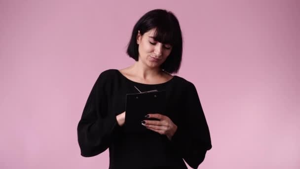 ピンクの背景の上にいくつかのメモを取る1人の女性の4Kビデオ 感情の概念 — ストック動画
