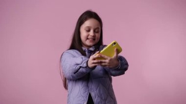 Pembe arka planda telefonu kullanan güzel bir kızın 4K videosu. Duyguların kavramı.