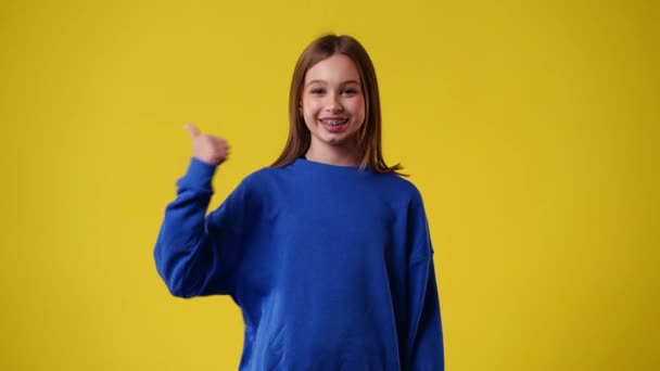 黄色の背景に親指を立てて微笑む1人の少女の4Kビデオ 感情の概念 — ストック動画