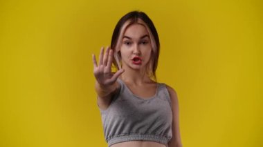 Sarı arka planda negatif yüz ifadesi olan birini durduran bir kızın 4K videosu. Duyguların kavramı.