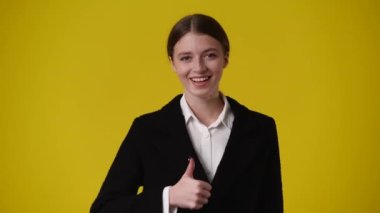 Bir kızın heyecanlandığı ve sarı arka planda başparmağını gösterdiği 4K videosu. Duyguların kavramı.