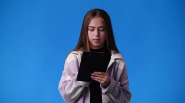 4k video of one girl which thinks and notes something with a pen on tablet over blue background. Concept of emotions.