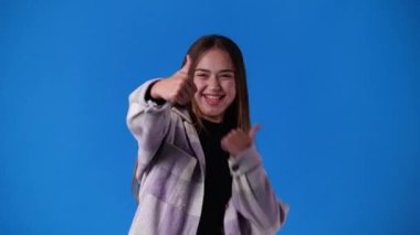 Mavi arka planda bir kızın baş parmağını gösterdiği 4K video. Duyguların kavramı.