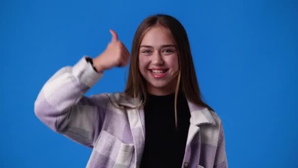 Відео Однієї Дівчини Вказує Камеру Показує Великі Пальці Синьому Фоні — стокове відео
