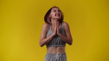 Sarı arka planda kurnaz bir yüz ifadesiyle el çırpan bir kızın 4k videosu. Duygular kavramı..