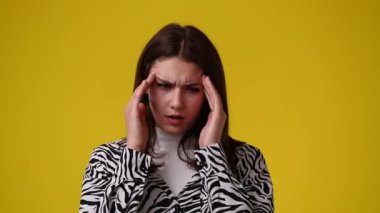Sarı arka planda başı ağrıyan bir kızın 4K videosu. Duyguların kavramı.