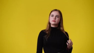 Sarı arka planda düşünceli yüz ifadesi olan bir kızın 4K videosu. Fikirleri olan kız kavramı.