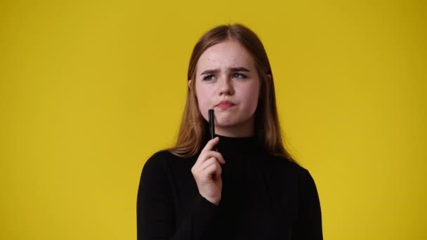 Vídeo Menina Com Expressão Facial Pensativa Com Caneta Fundo Amarelo — Vídeo de Stock