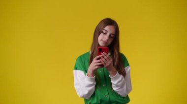 Sarı arka planda telefonunda mesaj bırakmaktan hoşlanan bir kızın 4K videosu. Duyguların kavramı.