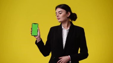 Elinde telefon olan ve sarı arka planda baş parmağını gösteren bir kızın 4K videosu. Duyguların kavramı.