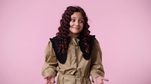 一个年轻女孩在粉色背景下怀疑并挥动双手的4K视频 情绪的概念 — 图库视频影像