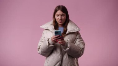 4k video of one girl using her phone over pink background. Concept of emotions.