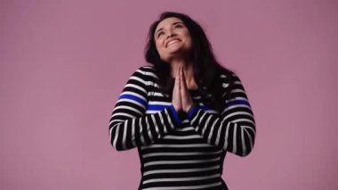 Pembe arka planda kurnaz bir yüz ifadesiyle yalvaran bir kızın 4K videosu. Fikirleri olan kız kavramı.