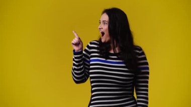 Sol tarafı işaret eden ve sarı arka planı gösteren bir kızın 4K videosu. Duygu kavramı.