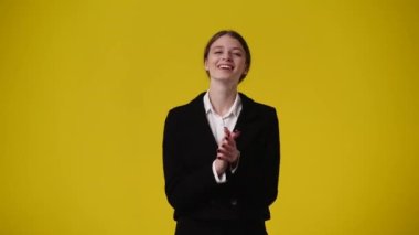 Sarı arka planda kurnaz bir yüz ifadesiyle el çırpan bir kızın 4k videosu. Duygular kavramı..