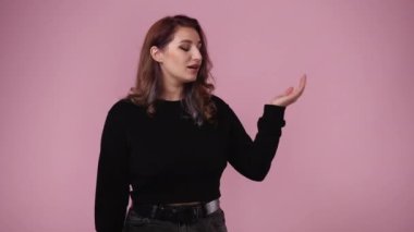 Bir kızın sağı işaret ettiği ve pembe arka planda baş parmağını gösterdiği 4K video. Duygu kavramı..