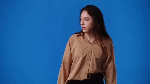 1人の女の子が左を向いて親指を青の背景の上に見せる4Kビデオ 感情の概念 — ストック動画